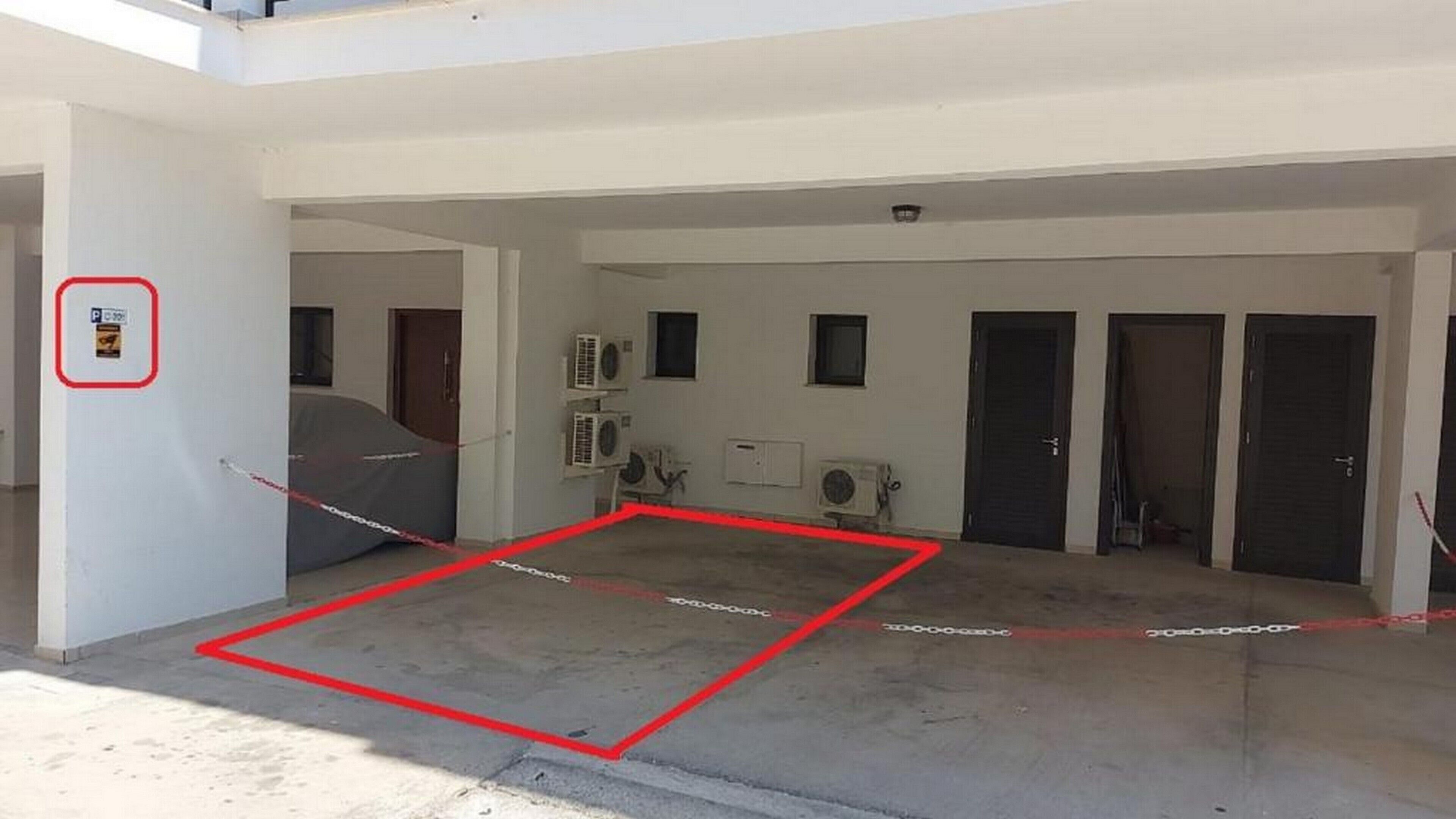 An open-plan area with a covered car and a red safety line on the floor.