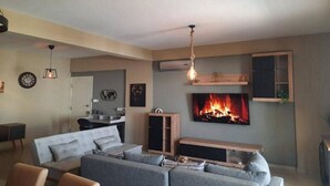 A modern living room with a grey sofa, a TV mounted on the wall, and a fireplace. - Paramount Gardens Resorts C201 (Tersefanou)