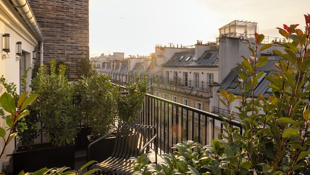 A balcony with a view of a cityscape, featuring a brick wall, potted plants, and a metal railing. - Hôtel Filigrane & Spa (Paris)