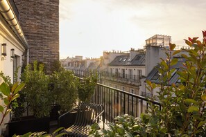 A balcony with a view of a cityscape, featuring a brick wall, potted plants, and a metal railing.