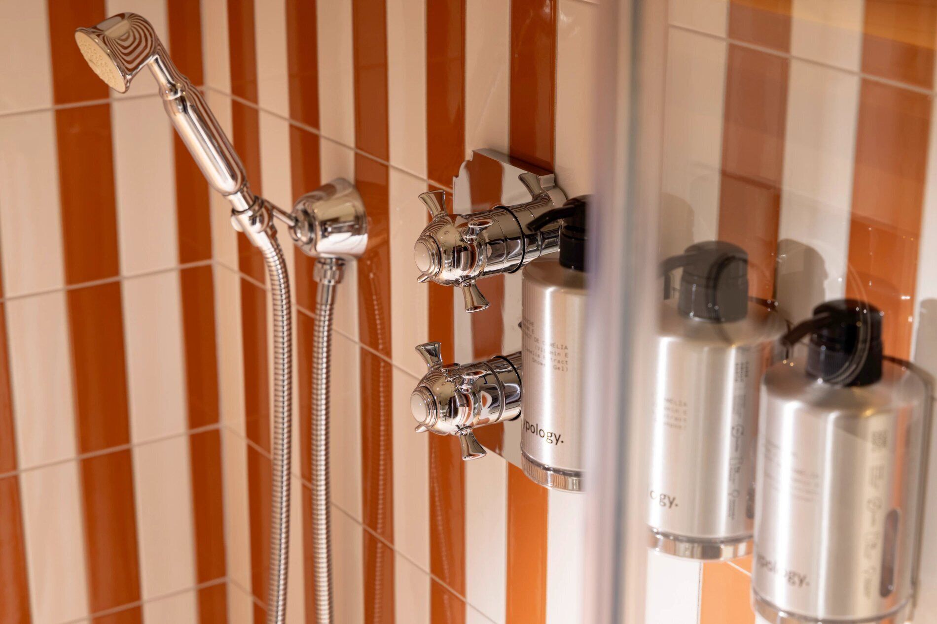 Een douche met meerdere douchetuiten en slangen, en flesjes toiletartikelen aan de muur.