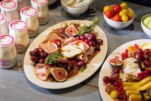 A table with various food items including meats, cheeses, fruits, and a bowl of cherry tomatoes.