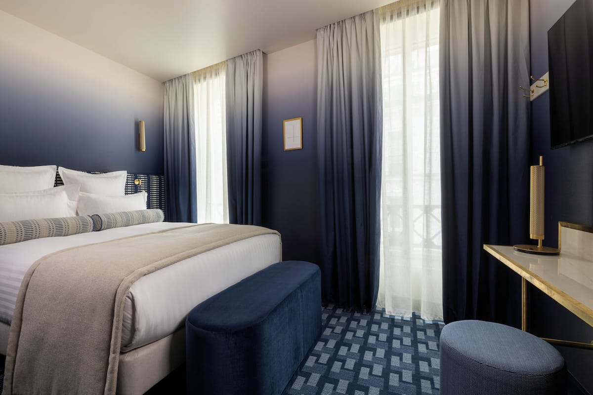 Habitación de hotel con cama, escritorio y ventana grande con cortinas.