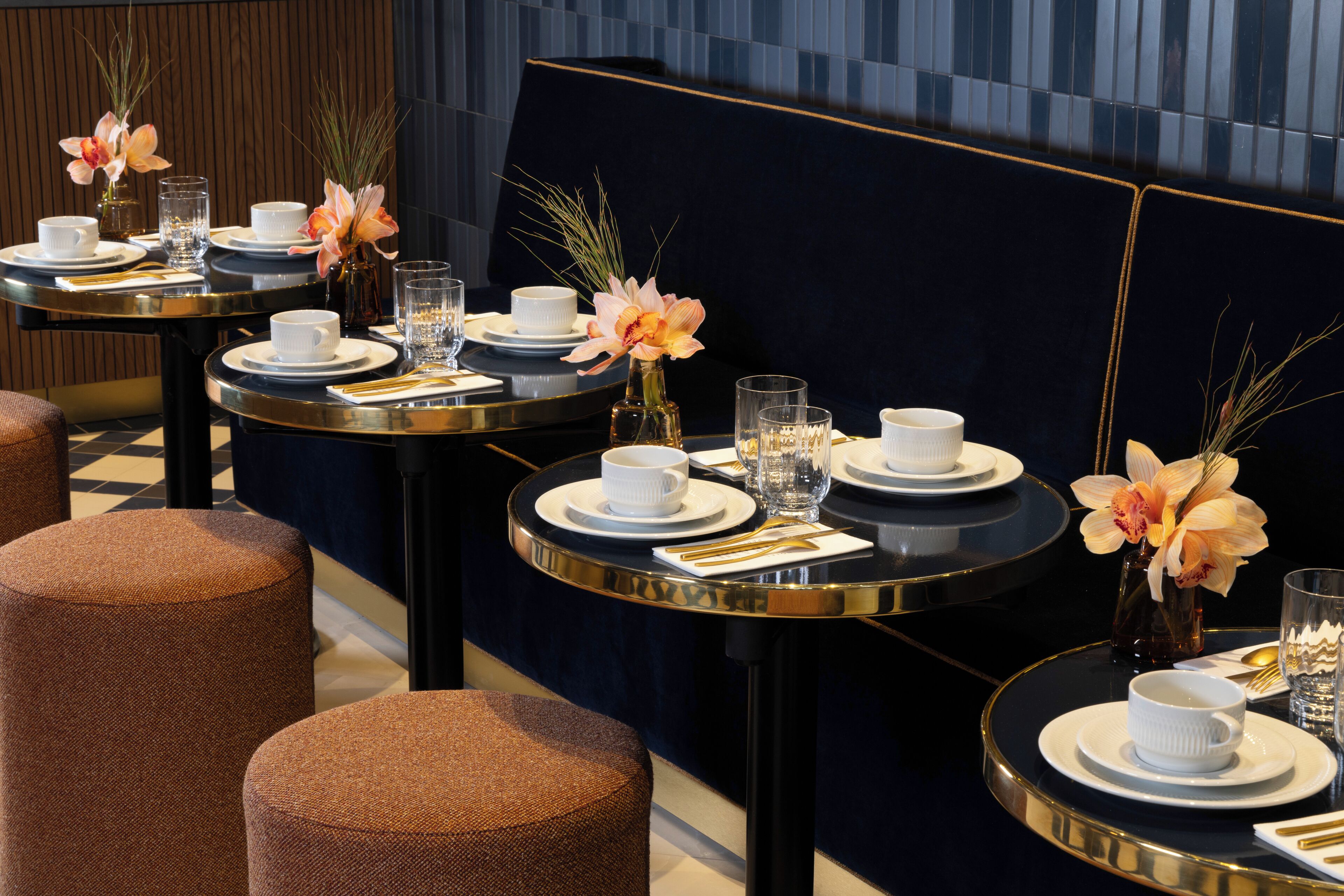A dining area with round tables set for service, featuring white dishes, gold cutlery, and floral centerpieces.