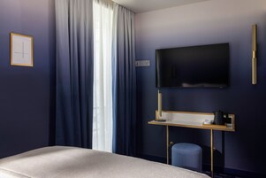 Habitación de hotel con cama, escritorio con televisor de pantalla plana, silla y ventana con cortinas.