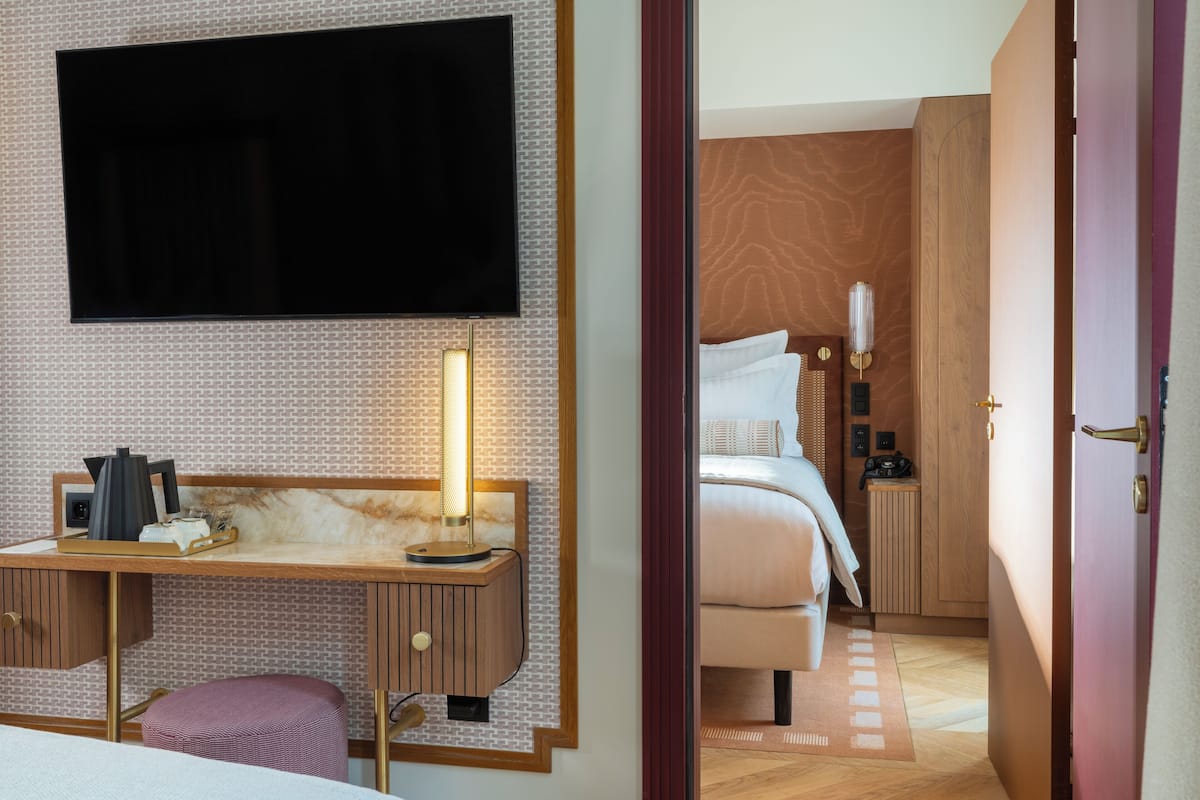 Habitación de hotel con televisor de pantalla plana en la pared, escritorio con lámpara, cama con cabecero y armario.