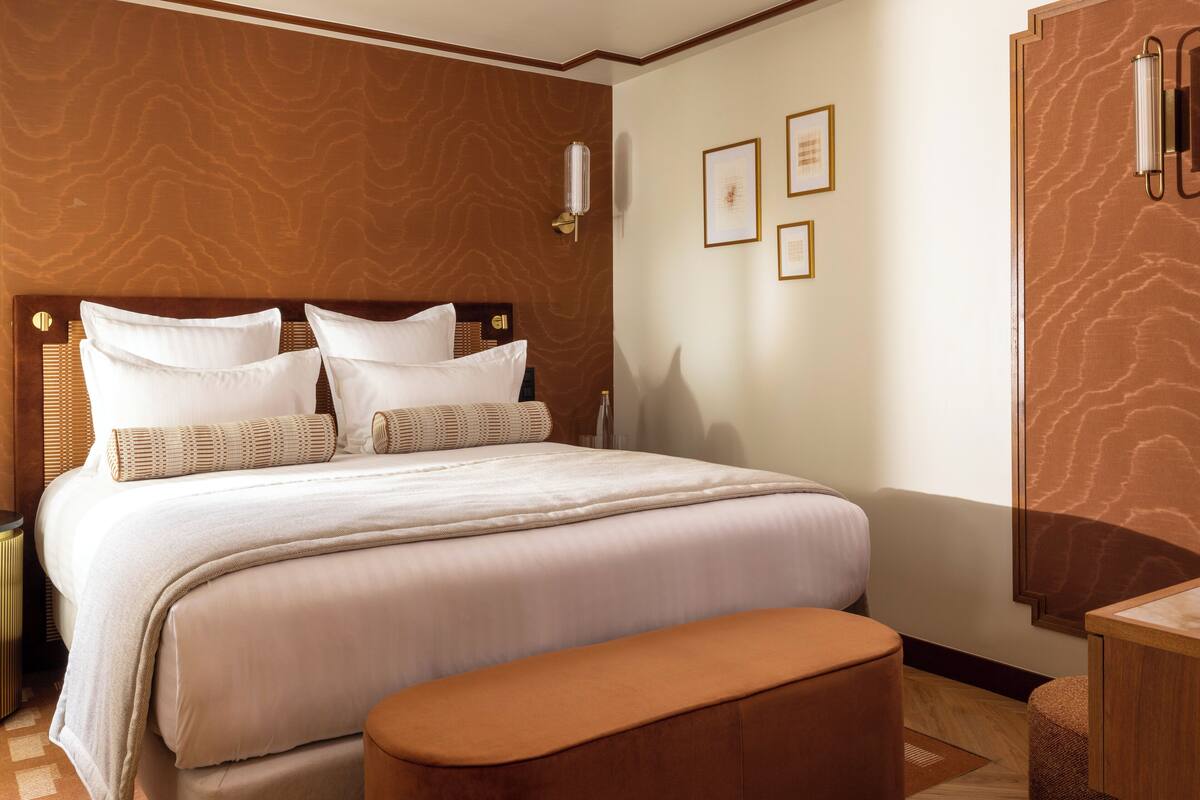 Una habitación de hotel con una cama grande, un cabecero de madera, una mesita de noche y un banco.
