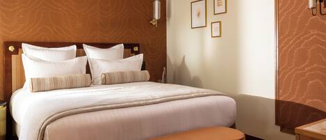 A hotel room with a large bed, a wooden headboard, a bedside table, and a bench.