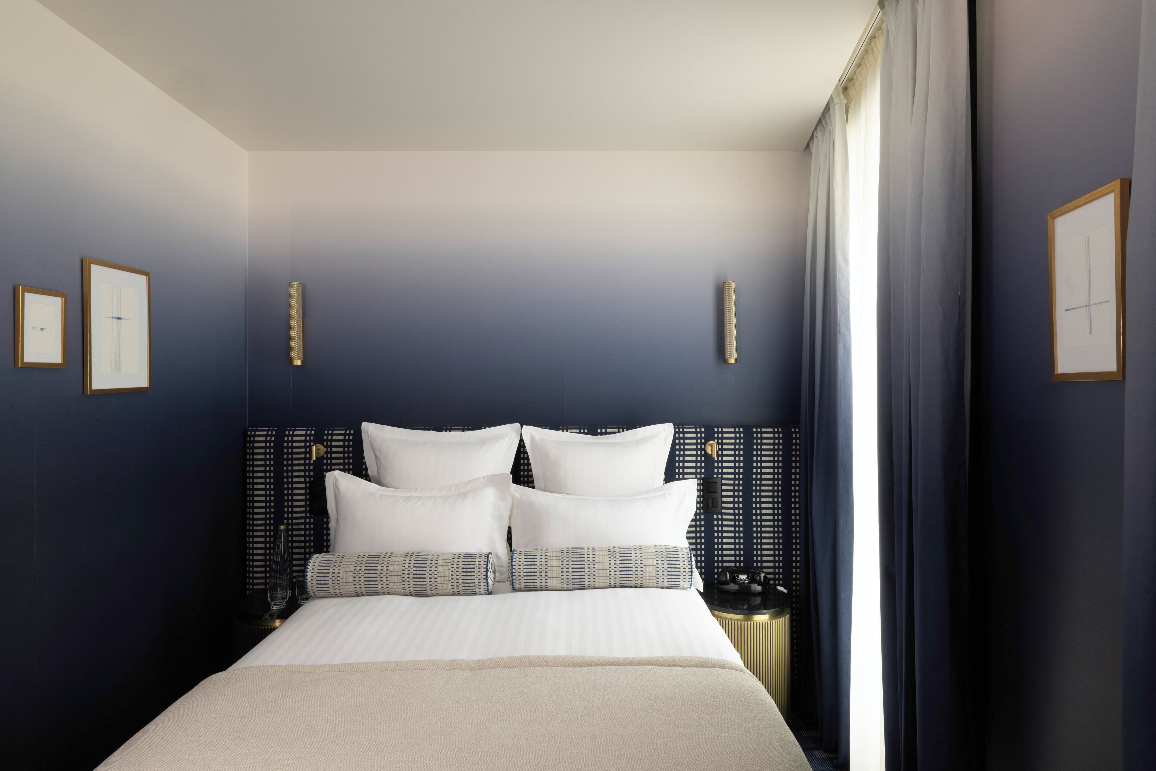 A modern hotel room with a large bed, dark walls, and a large window with curtains.