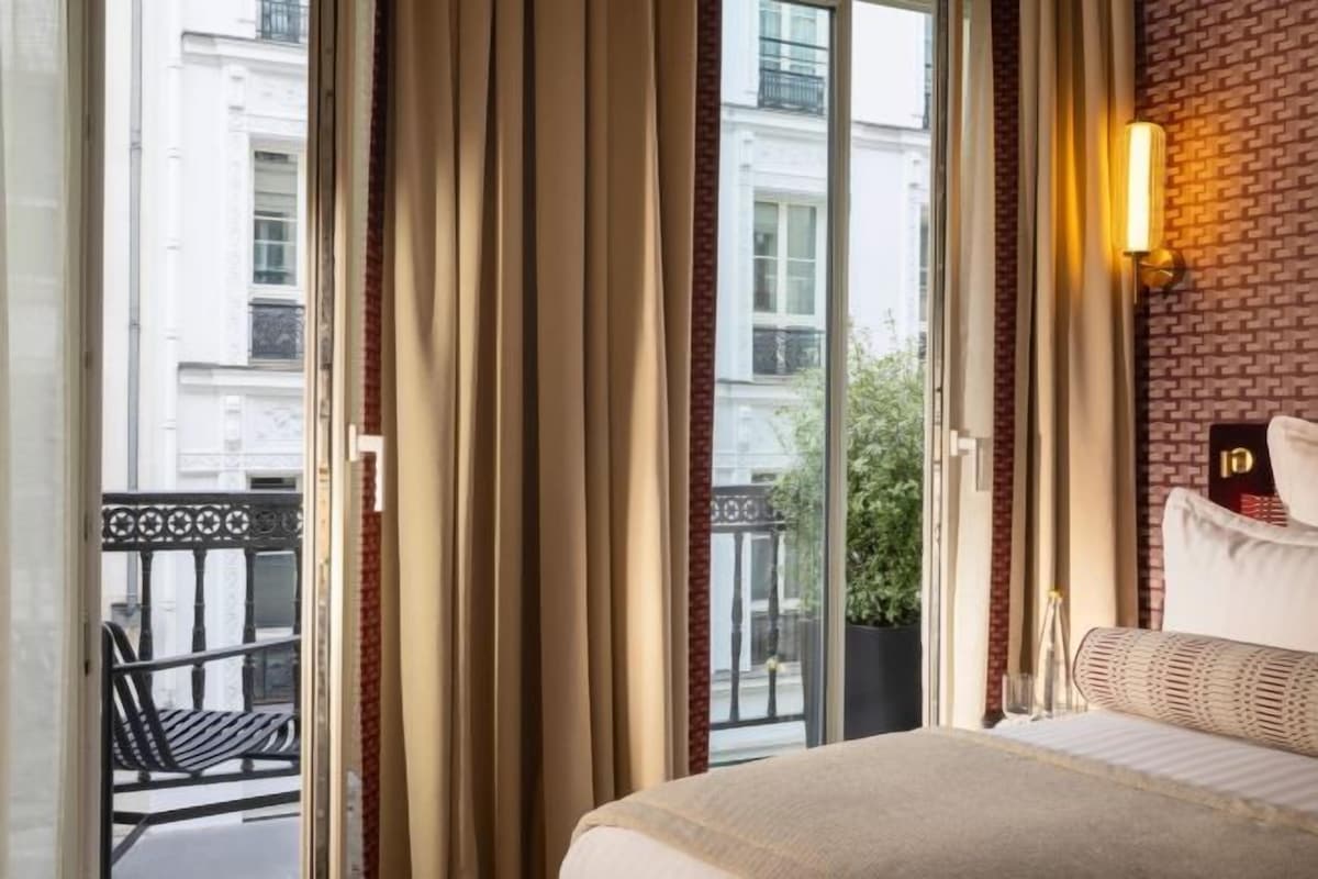Une chambre d’hôtel avec une grande fenêtre, un lit et une vue sur la rue et les bâtiments environnants.