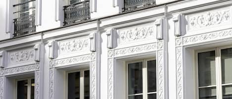 Fachada de edificio con detalles arquitectónicos blancos y ornamentados, múltiples ventanas y balcones de hierro forjado negro.