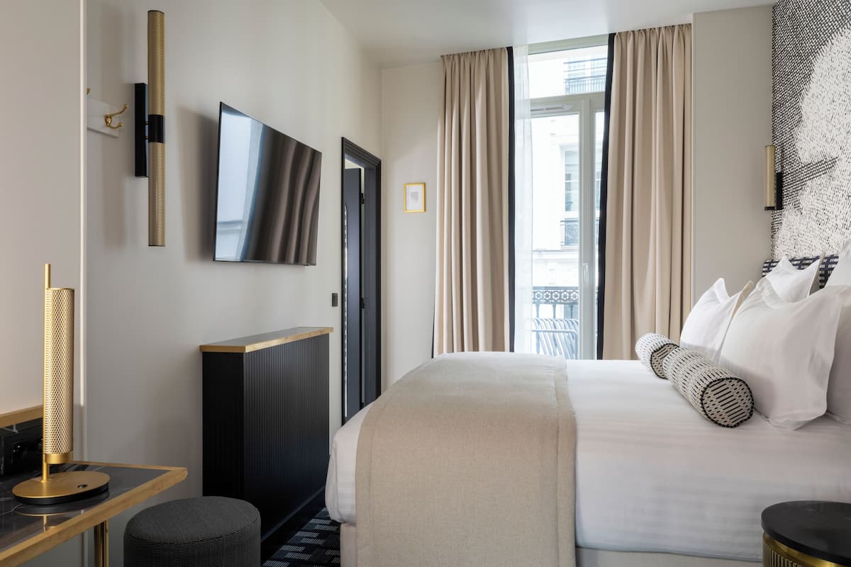 Una habitación de hotel con cama, escritorio, televisión y ventana con cortinas.