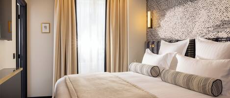 A hotel room with a large bed, beige curtains, a wall-mounted TV, and a patterned headboard.