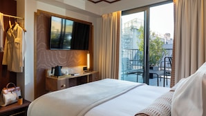 A hotel room with a large bed, a flat-screen TV mounted on the wall, a desk with a lamp, and a view of the city through a sliding glass door. - Hôtel Filigrane & Spa (Paris)