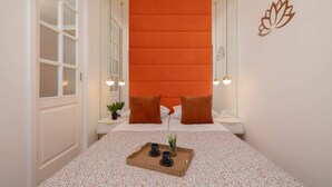 Une chambre à coucher avec un lit, deux tables de chevet, un plateau avec des tasses et une plante, et un mur orné d’un symbole de lotus.