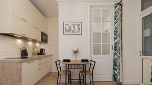 Une cuisine compacte avec un coin repas, dotée d’un crédence carrelée blanche, d’un four à micro-ondes, d’une machine à café et d’un tableau encadré au mur.