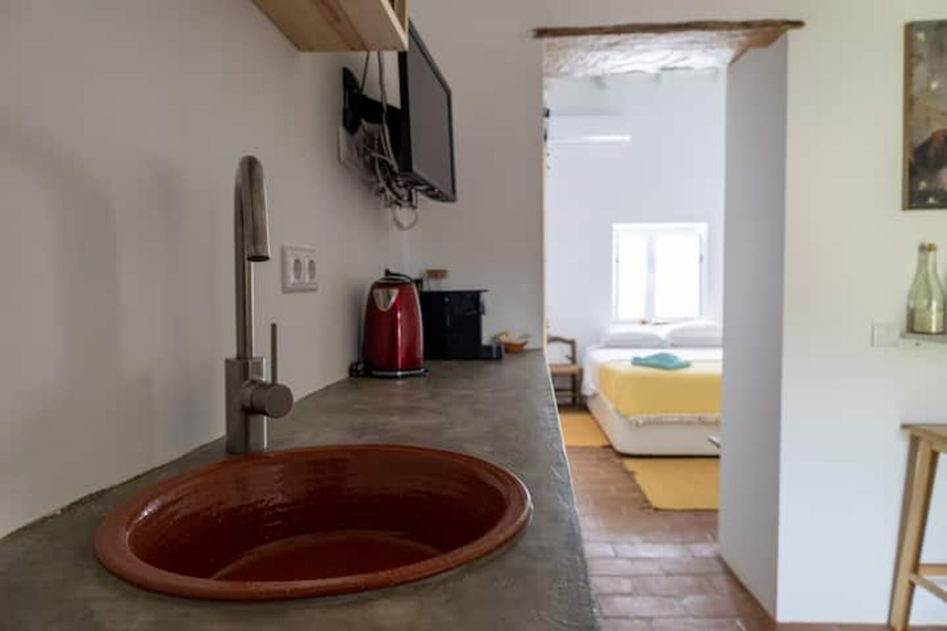 Una cocina con un tazón rojo grande, una cafetera y un televisor instalado en la pared.