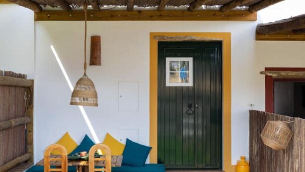A cozy room with a wooden ceiling, a green door, a small table with chairs, and a woven hanging light fixture.