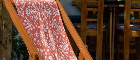 A wooden lounge chair with a patterned cushion, a wooden table, and chairs in a garden setting.