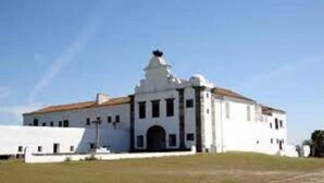 A white building with a central dome and a bell tower, surrounded by a grassy area.
