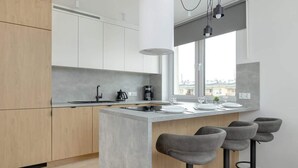 Una cocina moderna con una isla central, taburetes de bar y vistas a edificios a través de un ventanal grande.