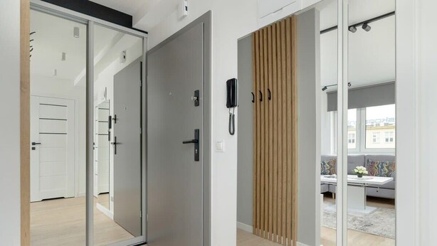 Habitación moderna con puerta de vidrio corredera que da a un balcón, pared de listones de madera y una pequeña mesa con un florero.
