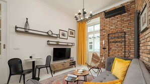 Ein modernes Wohnzimmer mit grauem Sofa, gelben Kissen, einem Fernseher und einer Ziegelwand.