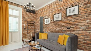Ein Wohnzimmer mit Backsteinwand, einem grauen Sofa mit gelben Kissen, einem Holztisch und einem Ledersessel, sowie einem gemusterten Teppich.