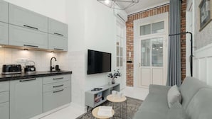 A modern kitchen with grey cabinets, a flat-screen TV, and a dining area with a grey sofa and a small round table.