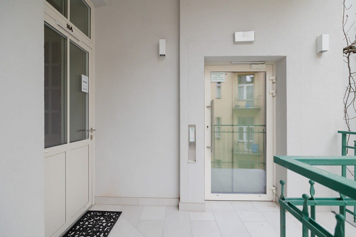 Un couloir étroit avec une porte donnant sur un balcon. Il y a une petite fenêtre sur la gauche et un luminaire fixé au mur au-dessus de la porte.