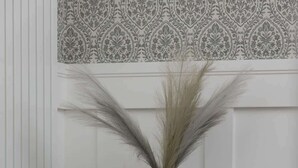 A dining table set with white plates, two wine glasses, and a vase with dried pampas grass.