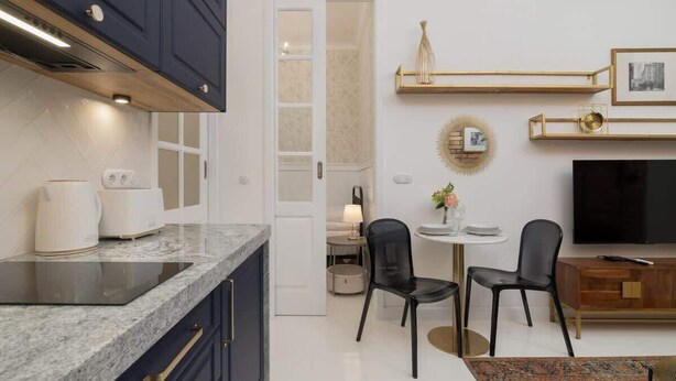 A modern kitchen with dark cabinets, a marble countertop, and a dining area with black chairs and a small table. - Stylish Apartment | Balcony and Air Conditioning (Kraków)