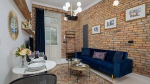 A living room with a blue sofa, a coffee table, and a dining area with a table set for two. - Stylish Apartment | Balcony and Air Conditioning (Kraków)