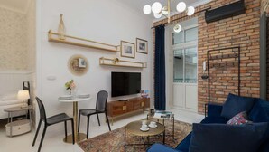 A modern living room with a blue sofa, a TV, a dining area with a table and chairs, and a brick accent wall. - Stylish Apartment | Balcony and Air Conditioning (Kraków)