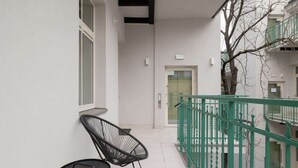 A narrow corridor with a green railing, a door at the end, and two black chairs against the wall. - Tasteful Apartment with Balcony | Air Conditioning | Close to the Center (Kraków)