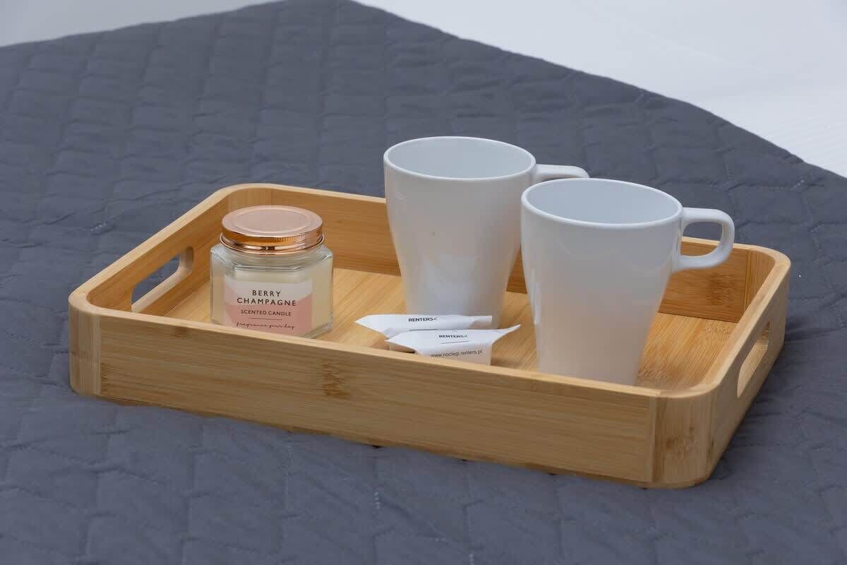 A wooden tray with a bottle of scented candle, two white mugs, and a small packet.
