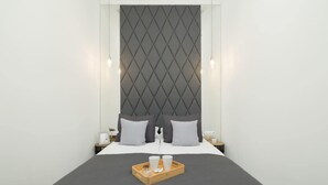 A modern hotel room with a large bed, a headboard with a diamond pattern, two bedside tables with lamps, and a tray with a cup and a bottle on the bed. - Tasteful Apartment with Balcony | Air Conditioning | Close to the Center (Kraków)