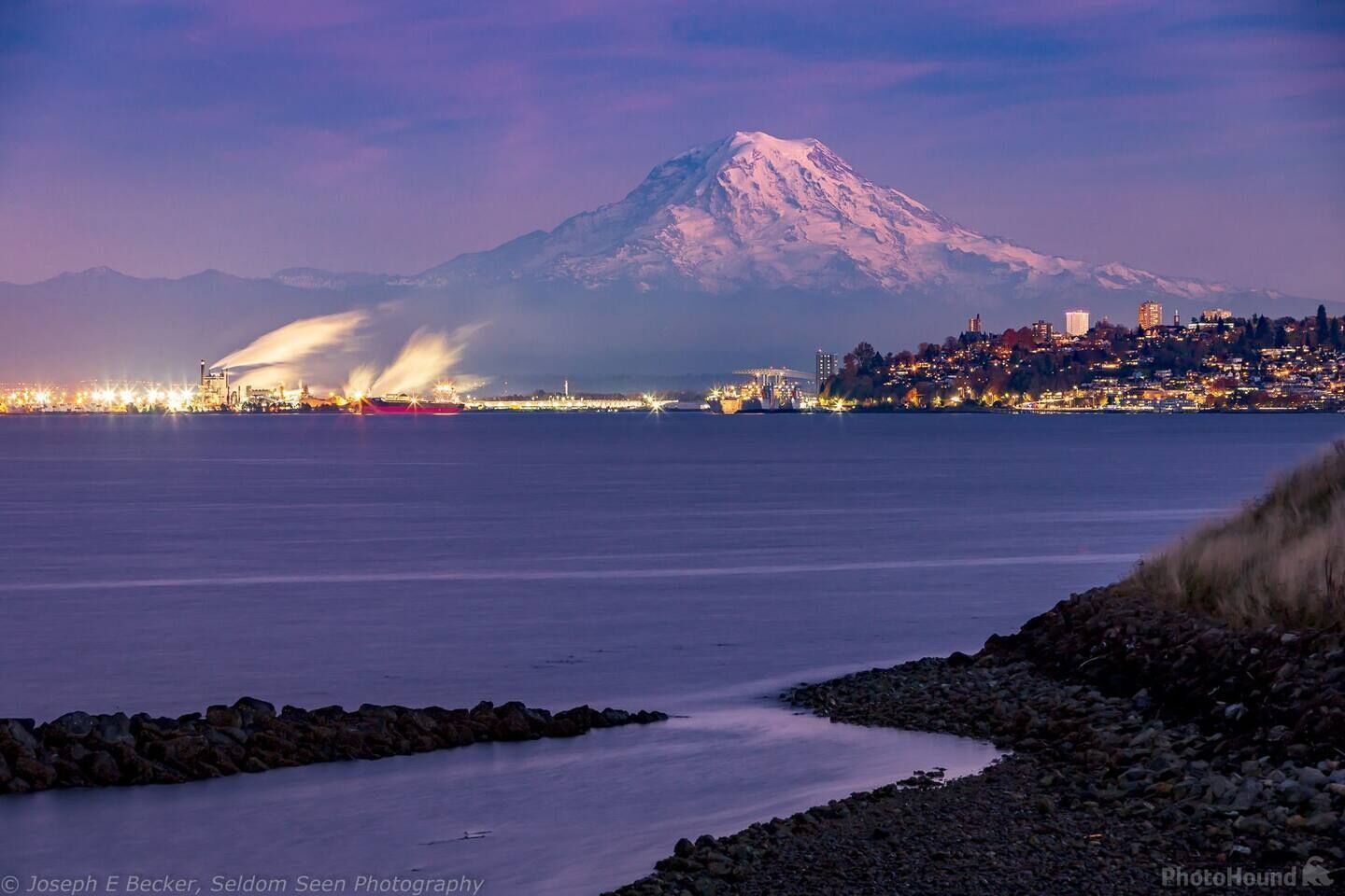 A coastal cityscape with a prominent snow-capped mountain in the background.