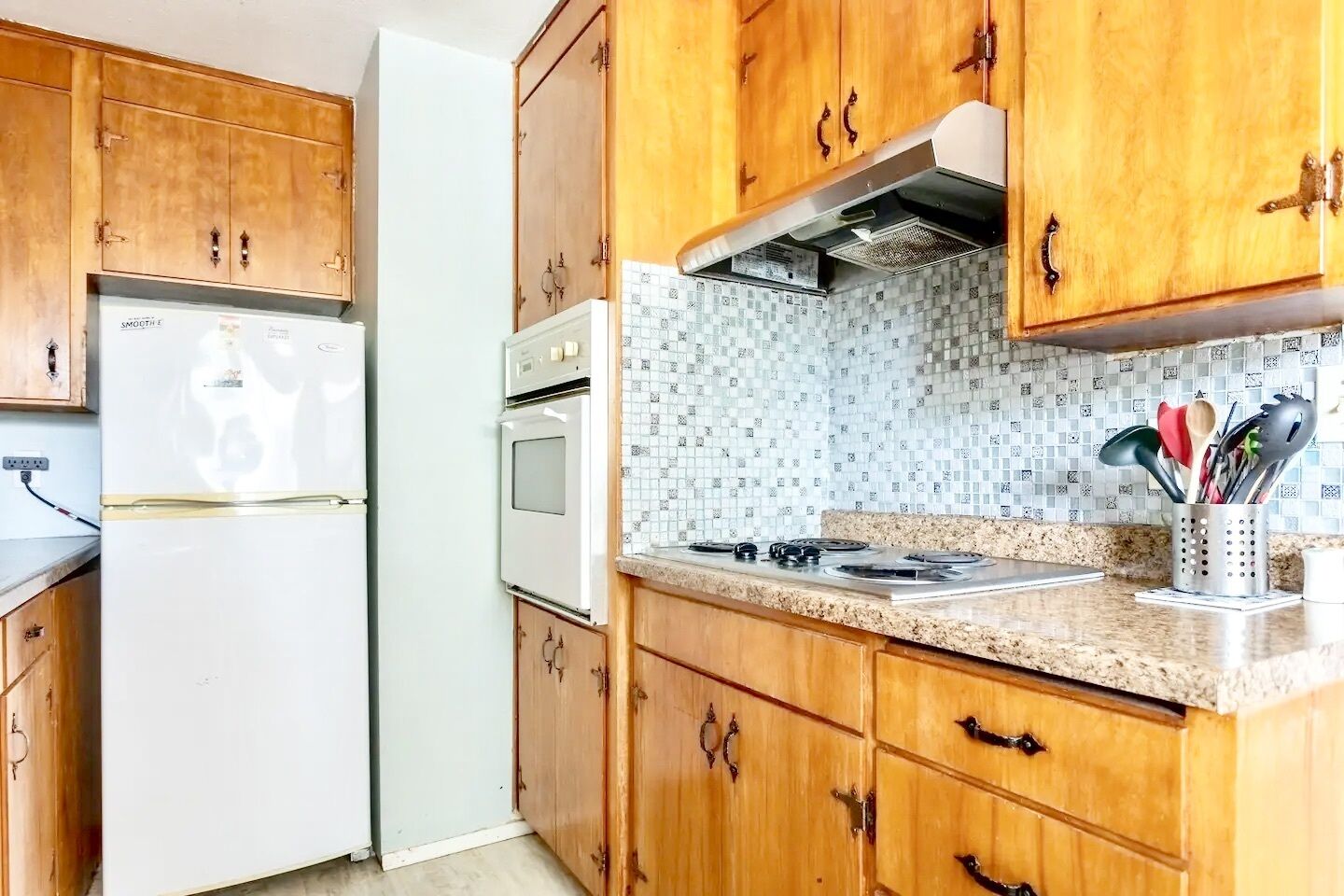 Eine Küche mit Holzausstattung, einem weißen Kühlschrank, einem Herd und einer gefliesten Spritzschutzwand.
