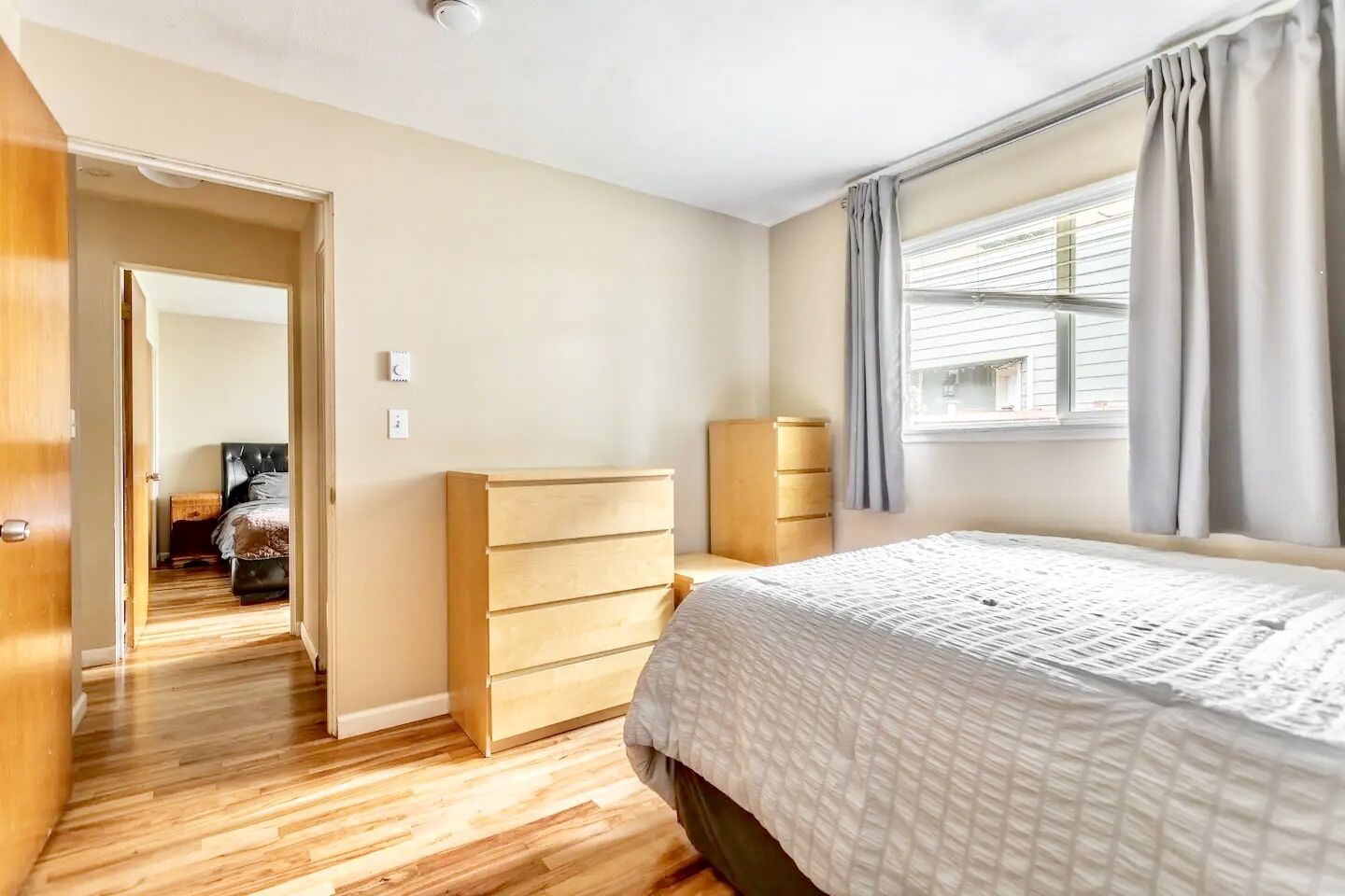 Un dormitorio con cama, cómoda de madera y ventana con cortinas.