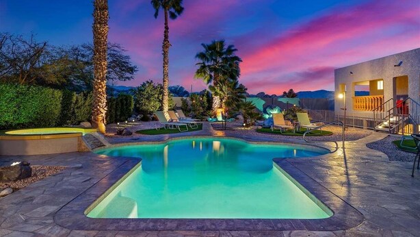 A swimming pool with lounge chairs and palm trees, surrounded by a landscaped garden and a building with a modern design.