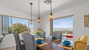 A dining area with a wooden table, grey and yellow chairs, and pendant lights.