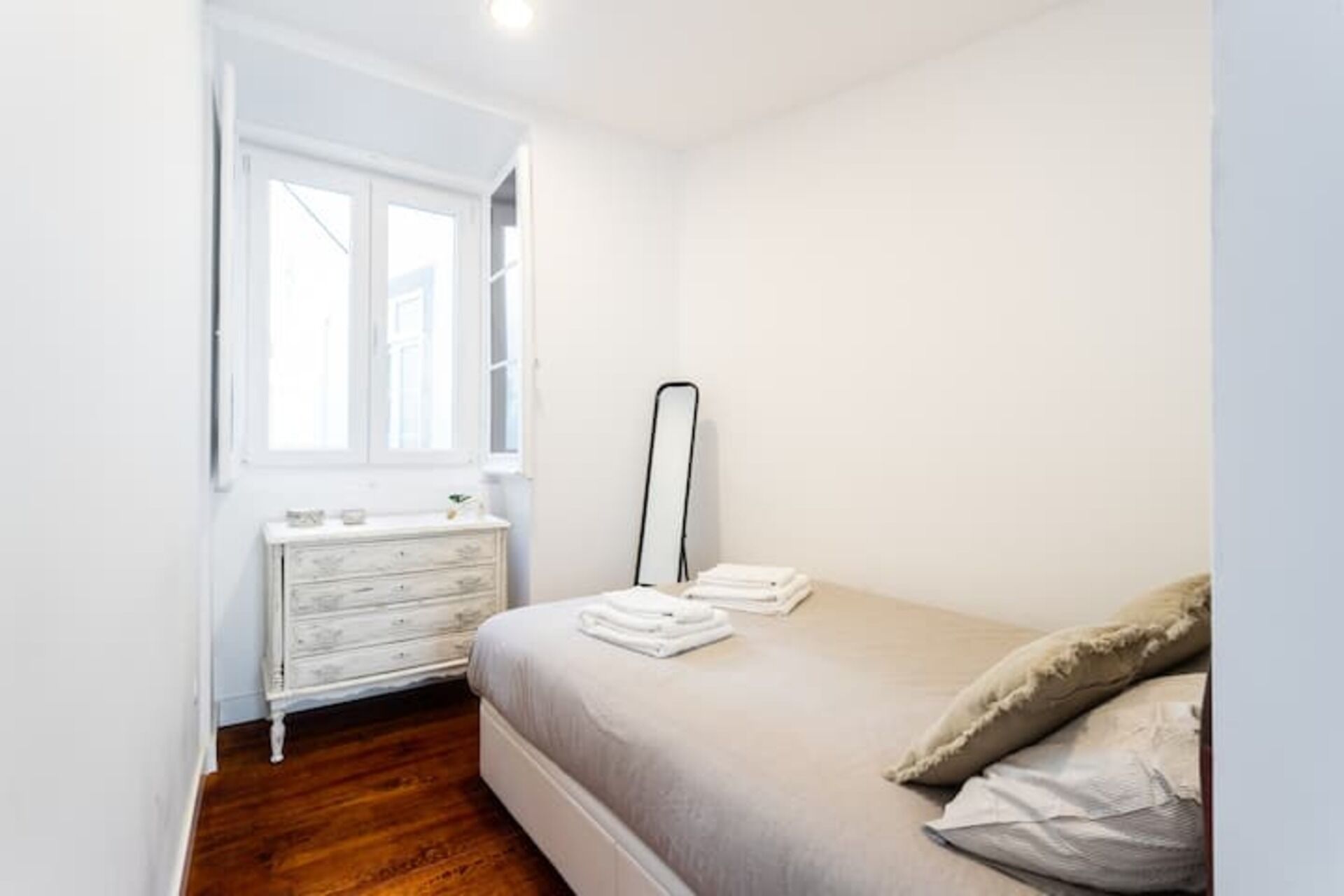 Une chambre à coucher avec un lit, une commode, un miroir et une fenêtre.