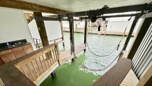 A wooden deck with a green pool, a wooden bench, and a metal structure above.