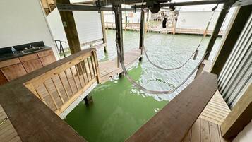 A wooden deck with a green pool, a wooden bench, and a metal structure above.