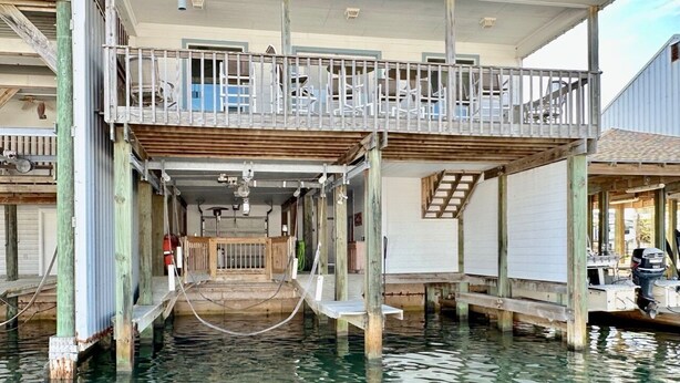 A waterfront house with a balcony, wooden deck, and a dock extending into the water.
