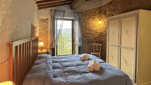 A bedroom with a large bed, stone walls, a wooden ceiling, and a window with a view. - Borgo Tignano (Volterra)