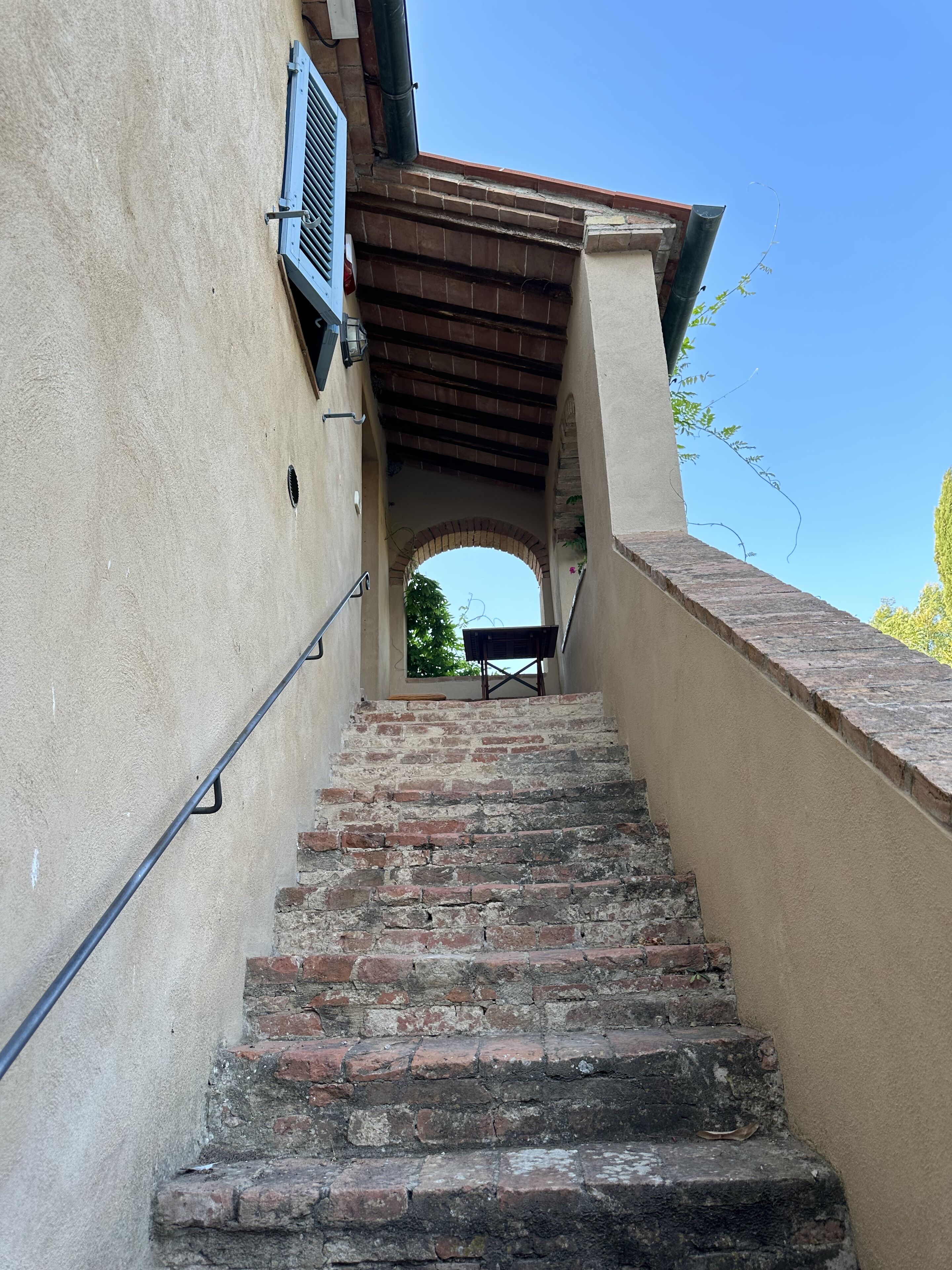 A staircase leading to an archway, with a metal handrail on the left and a wooden beam on the right.