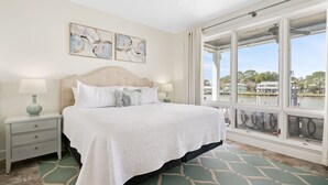 A bedroom with a large bed, two bedside tables, and a view of a body of water through large windows.