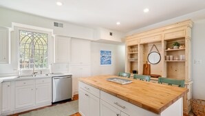 A kitchen with white cabinets, a wooden countertop, and a dining area with green chairs.